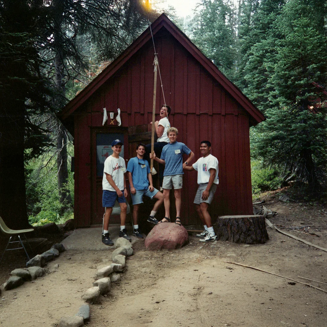 Vintage photo of Silver Lake Band Camp campers posing outside a rustic red cabin surrounded by pine trees.
