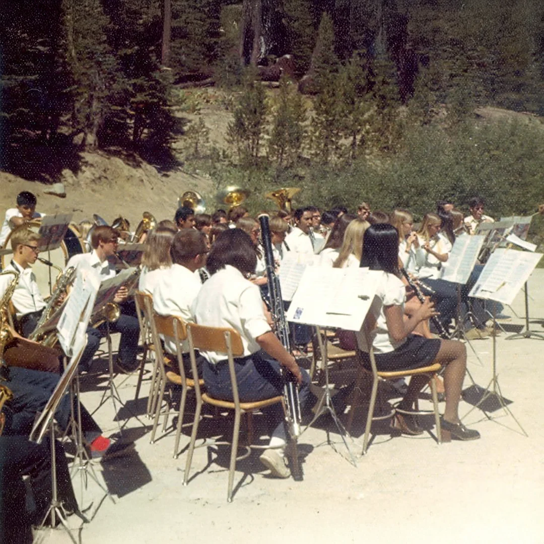 Vintage photo of a large Silver Lake Band Camp ensemble rehearsing outdoors with music stands and instruments surrounded by pine trees.
