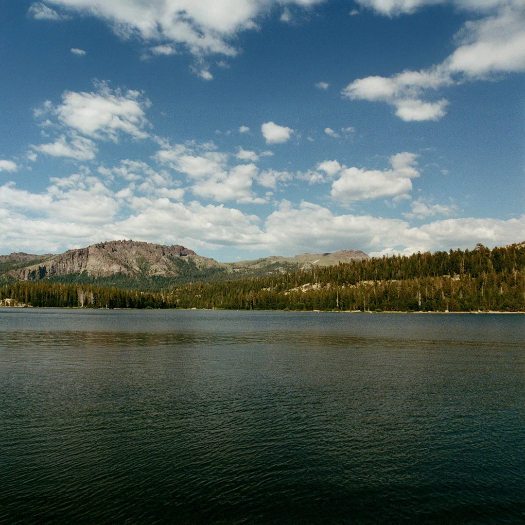 Wide view of Lake Tahoe with calm water, pine trees, and surrounding mountains under a partly cloudy sky near Silver Lake Band Camp.
